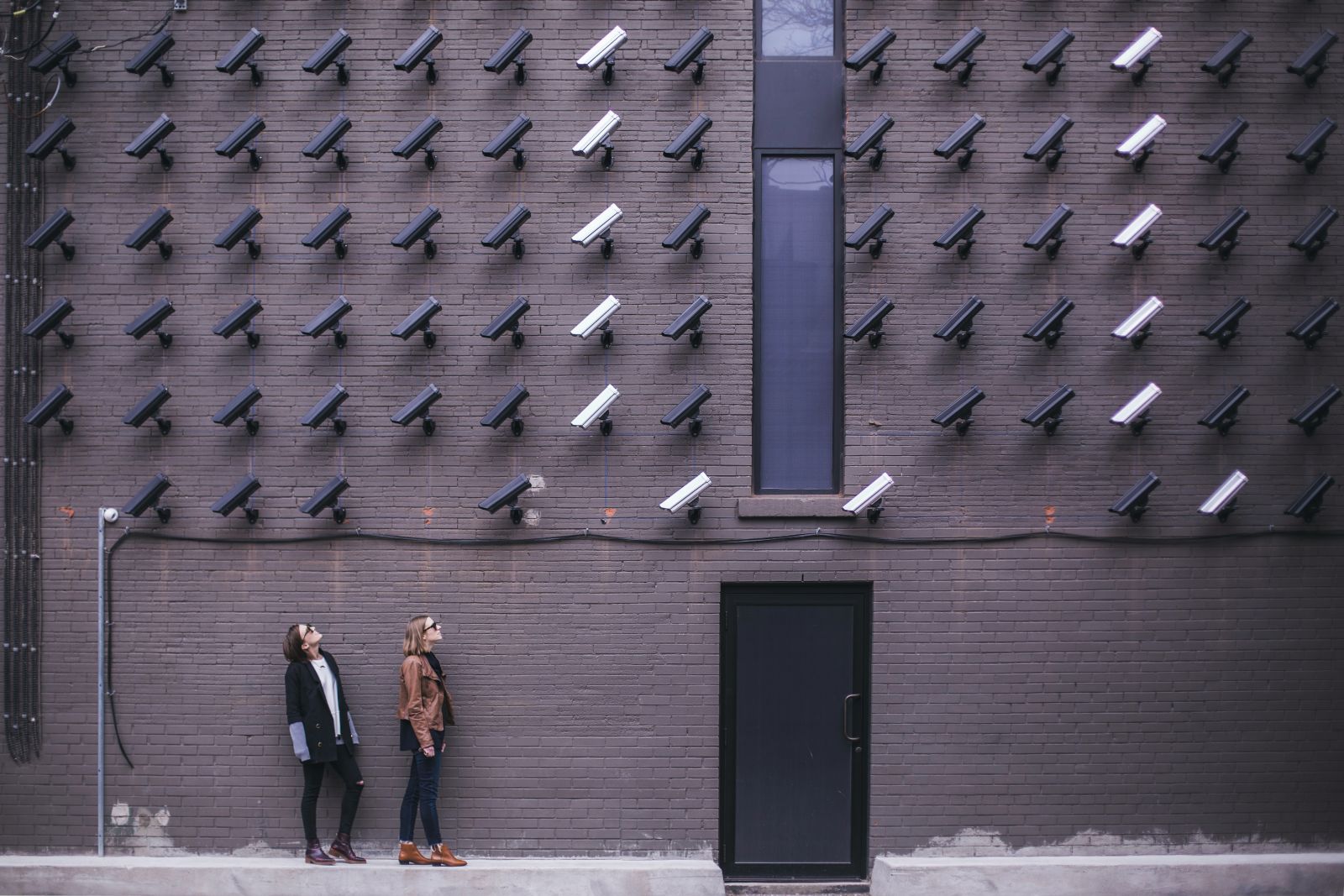 Two people looking up at a wall of dozens of security cameras facing them.